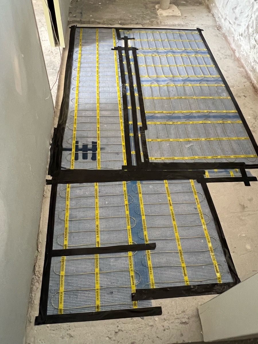 Heating mats taped to a bathroom substrate, shaped around a floor penetration and ready for the finish