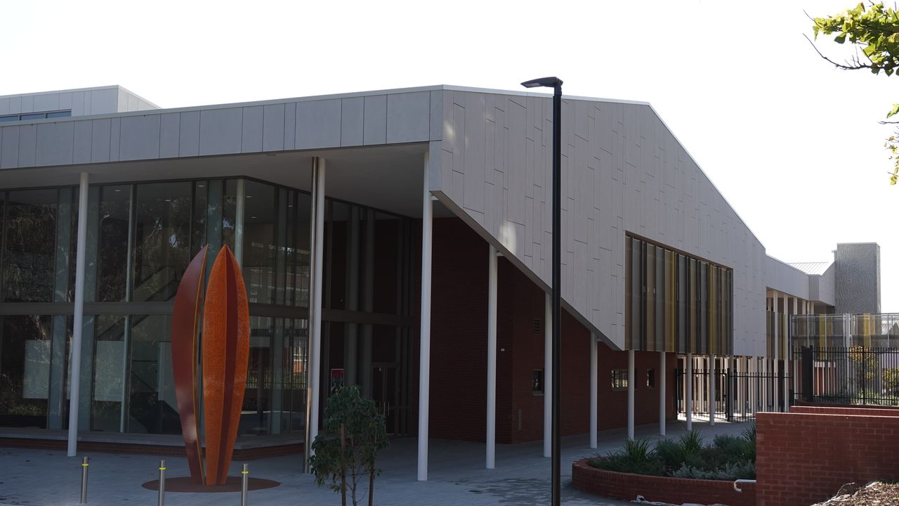 Contemporary building entry with a glazed lobby, white columns, and a sculptural screen