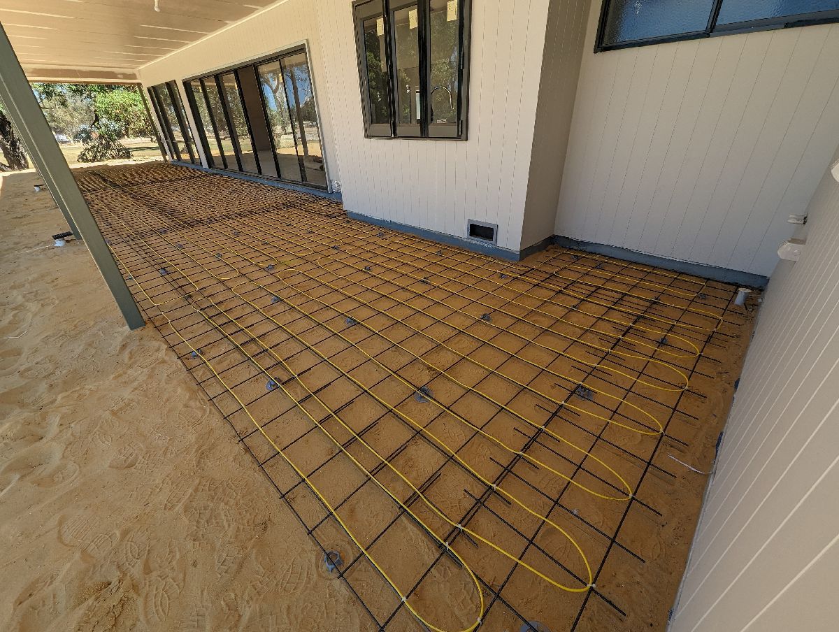 Yellow electric heating cables laid in loops and fixed to reinforcing mesh on an outdoor verandah slab