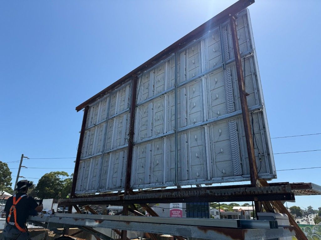 Steel structure and rear of a large outdoor LED billboard, with a technician on the platform