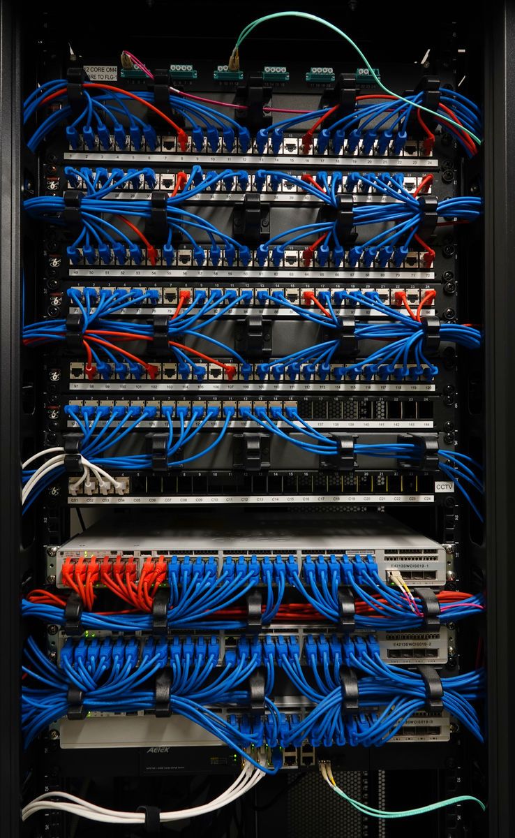 Network cabinet with neatly dressed blue and red patch leads across stacked panels and switches