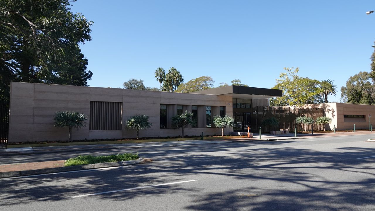 Single-storey commercial building with a rendered facade, vertical louvres, and a planted street frontage